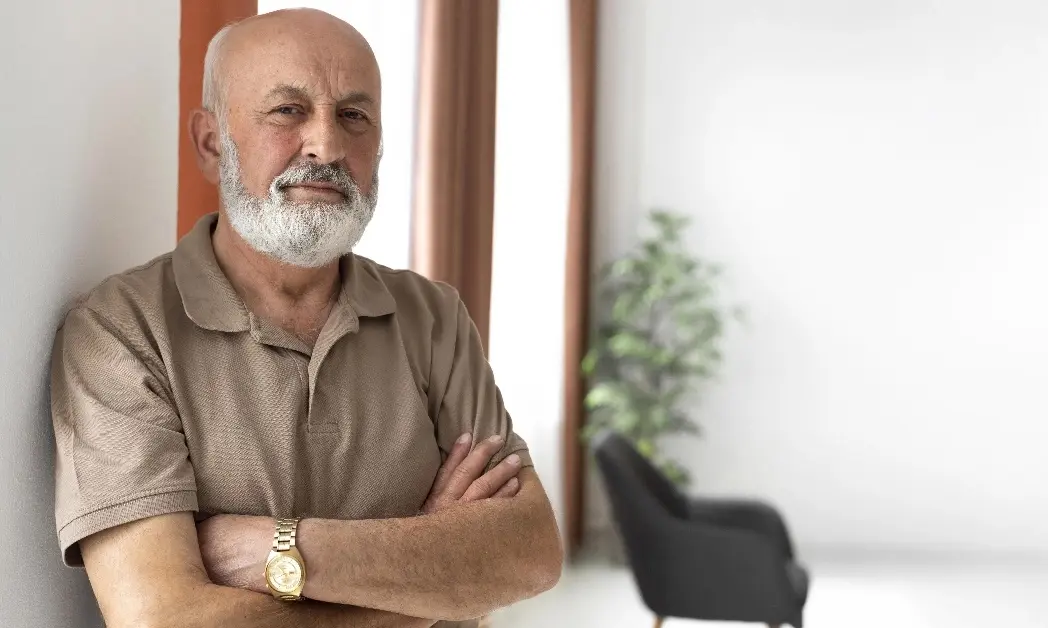 Älterer Mann mit verschränkten Armen lehnt an einer Wand