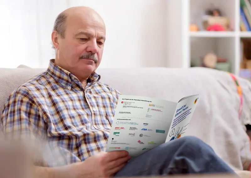 Älterer Mann sitzt auf dem Sofa und liest eine Broschüre