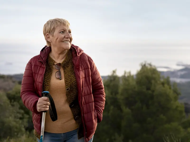 Ältere Frau mit Wanderstock lächelt auf einem Aussichtspunkt über dem Meer